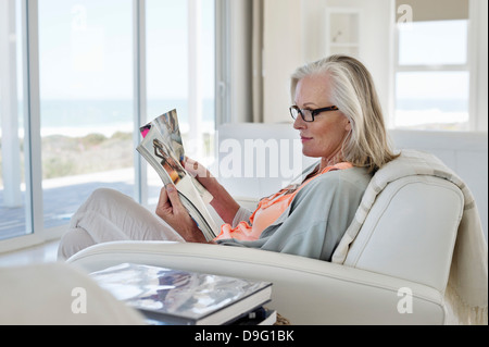 Femme assise sur un canapé et lit un magazine à la maison Banque D'Images