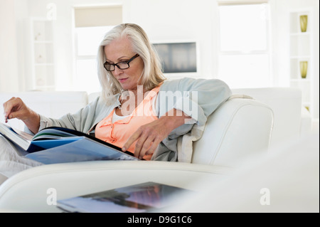 Femme assise sur un canapé et la lecture d'un livre à la maison Banque D'Images