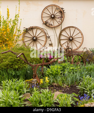 3 anciennes roues de chariot en bois fixé au mur en fer rouille rural jardin avec charrue charrue ou parmi les fleurs et plantes Banque D'Images