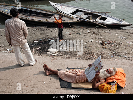 Sadhu lisant le journal, Garçon jouant avec un cerf-volant au bord du Gange. Varanasi, Benares, Uttar Pradesh, Inde Banque D'Images