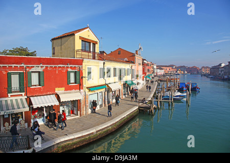 Les gens qui marchent le long de la chaussée et de vieux bâtiments colorés et bateaux amarrés sur le canal à l'île de Murano Venise Italie Banque D'Images