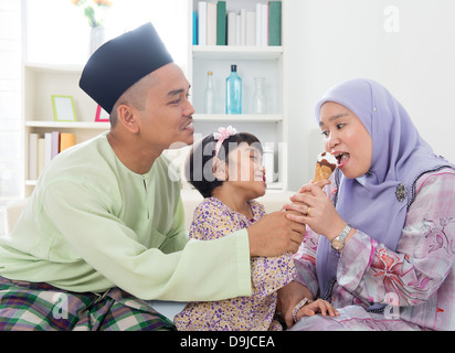 Se nourrir de la crème glacée. Jeune fille musulmane allaite une glace. Belle famille Asie du Sud-Est vivant de vie à la maison. Banque D'Images