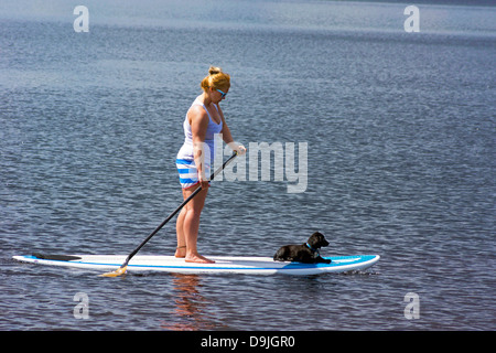 Une femme sur le Loch Insh paddleboarding avec son chien. Banque D'Images