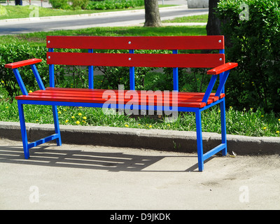 Banc rouge vide dans un parc sur un fond d'herbe verte Banque D'Images