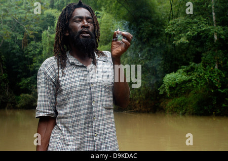 Rasta Man smoking a cigarette de marijuana à bamboo rafting, grand fleuve, Jamaïque Banque D'Images