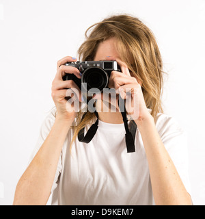 Une jeune femme photographe avec de longs cheveux blonds à l'aide d'un petit Fuji X100s appareil photo numérique Banque D'Images