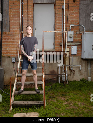 Portrait of young tattooed man standing on staircase Banque D'Images