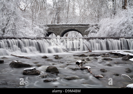 Arbres couverts de neige qui encadrent un pont de pierre et Cascade en hiver, dans le parc, Sharon Woods, le sud-ouest de l'Ohio, USA Banque D'Images