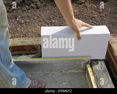 Builder / travailleur de la construction travaillant sur un mur de briques dans thermalite cimentation Banque D'Images