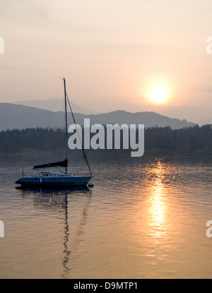 Une vue verticale d'un yacht solitaire sur Windermere avec arbres bois et collines au loin et soleil sur les collines. Banque D'Images