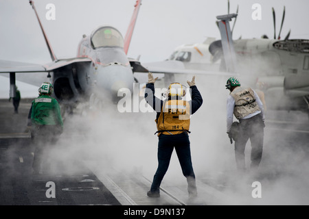 L'Aviation de l'US Navy un maître de Manœuvre dirige un F/A-18C Hornet à une catapulte sur le pont du porte-avions USS Carl Vinson, 11 juin 2013 au large de la côte de Californie du Sud. Banque D'Images