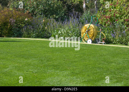 Tuyau de jardin mobile sur pelouse verte en jardin anglais. Banque D'Images