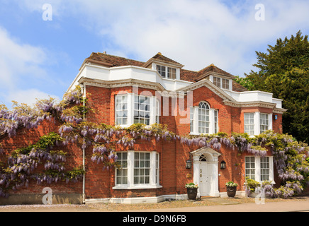 Wisteria floribunda autour d'un croissant rouge-brique maison géorgienne/dans un village pittoresque. Lavenham Suffolk Angleterre Royaume-uni Grande-Bretagne Banque D'Images