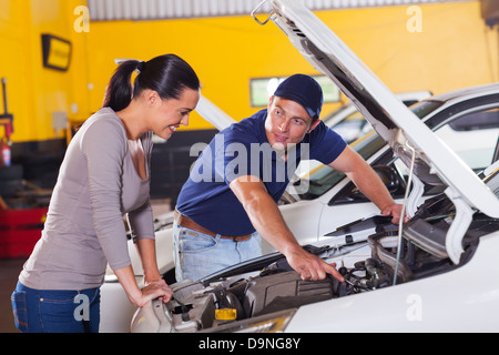 Friendly mechanic montrant sa voiture à la clientèle féminine problème dans garage Banque D'Images