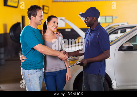 Technicien automobile de l'Afrique de l'établissement de liaison avec jeune couple en garage Banque D'Images