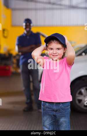 Cute little girl wearing auto Mechanic's cap dans l'atelier de réparation Banque D'Images