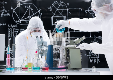 Vue générale de deux personnes manipulant des liquides colorés et d'outils de laboratoire sur une table de labo avec un tableau noir sur l'arrière-plan Banque D'Images