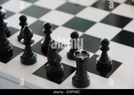 Cette image présente une configuration de jeu d'échecs classique avec un échiquier noir et blanc. Les pièces, y compris les tours noires et blanches (tours), sont disposées dans leurs positions de départ standard, les joueurs se préparant à une bataille stratégique. Les échecs, un jeu d'adresse et d'intellect, se jouent entre deux adversaires, chacun contrôlant 16 pièces, visant à mettre le roi de l'adversaire en échec et mat. Banque D'Images