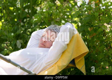 Femme mature avec poils blancs dormir sur une chaise longue dans son jardin. Banque D'Images