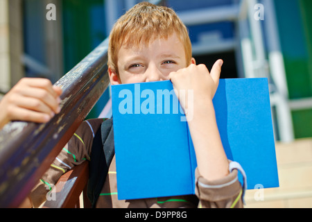 Jeune garçon secret avec livre en face de l'école Banque D'Images