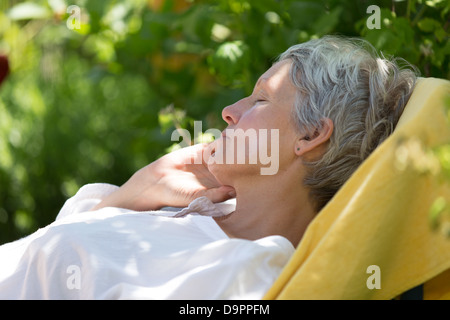 Femme âgée de poils blancs de dormir sur une chaise longue dans son jardin. Banque D'Images