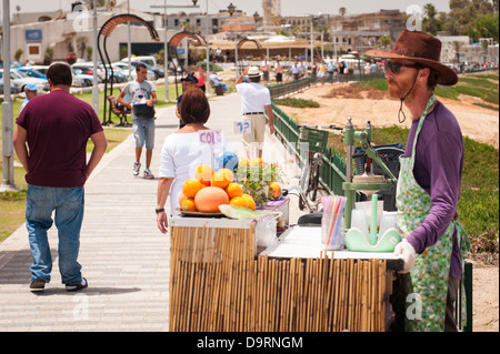 Israël Jaffa Yaf fruits frais jus boissons sur la promenade du vendeur portant chapeau de cow-boy stetson tablier vert oranges pamplemousses touristes gens barbe Banque D'Images