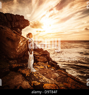 Photographe belle femme debout sur rocky seashore et profiter du coucher du soleil, voyage aventure en Afrique du Sud, le tourisme concept Banque D'Images