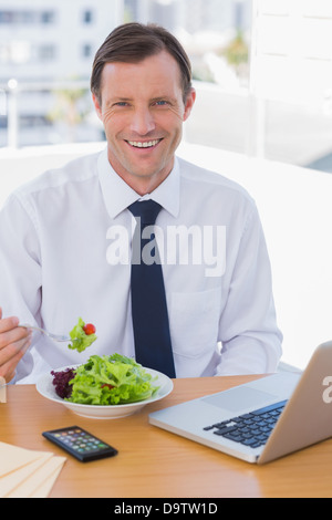 Cheerful businessman eating a salad sur son bureau Banque D'Images