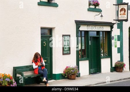 Une femme assise sur un banc à l'extérieur d'une boutique à la recherche de son appareil photo;Ballyvaughan comté de Clare Irlande Banque D'Images