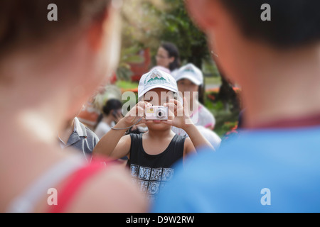 Une jeune fille prend une pciture de deux touristes dans le parc de la Citadelle impériale, Hue, Vietnam, Asie du Sud Est. Banque D'Images