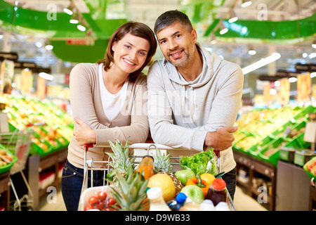 Image de l'heureux couple avec panier remplis de produits looking at camera in supermarket Banque D'Images