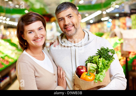 Image de l'heureux couple avec plein de produits the paperbag looking at camera in supermarket Banque D'Images