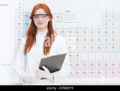 Close-up of young beautiful female scientist holding un presse-papiers dans ses bras, avec tableau périodique en arrière-plan Banque D'Images