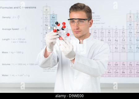 Close-up of handsome Young Scientist habillés en uniforme blanc l'étude de la structure moléculaire, avec tableau périodique en arrière-plan Banque D'Images