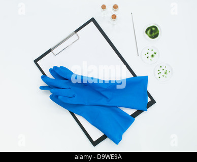 Gants de laboratoire bleu sur le dessus d'un clip vide-pension à côté de trois petites bouteilles avec un liquide transparent et trois plats de pétri contai Banque D'Images