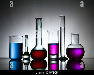 Vue latérale de différentes tailles et formes de verrerie de laboratoire, rempli de substances colorées contre un arrière-plan gris gradient portant sur une surface réfléchissante Banque D'Images