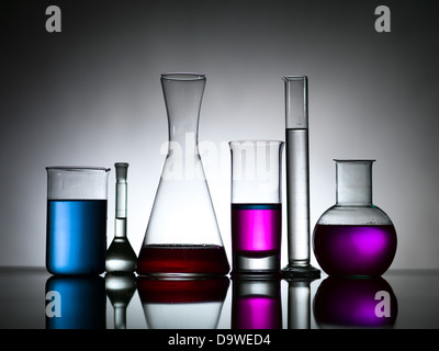 Vue latérale de différentes tailles et formes de verrerie de laboratoire, rempli de substances colorées contre un arrière-plan gris gradient portant sur une surface réfléchissante Banque D'Images