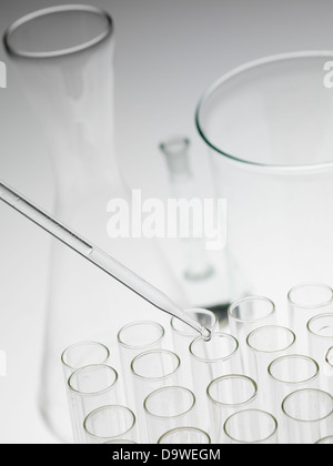 Background gris avec verrerie de laboratoire avec pipette dropping d'échantillon dans un tube à essai avec un bécher et une bouteille dans l'arrière-plan enlermeyer Banque D'Images