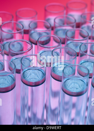 Vue aérienne, macro de tubes à essai remplis de substance flottant foncé transparent en liquide incolore, contre un dégradé rose et fond violet Banque D'Images