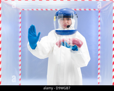 Femme dans un biohazard costume avec un échantillon de viande dans sa main gantée tenant de son autre main, dans un geste d'arrêter indiquant que t Banque D'Images