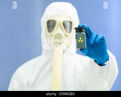 Personne en danger bio costume et masque à gaz tenant un isotope radioactif d'échantillon dans un petit pot en plastique vert Banque D'Images