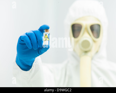Personne en danger bio costume et masque à gaz tenant un isotope radioactif d'échantillon dans un flacon incolore transparent Banque D'Images
