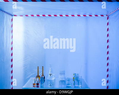 Les contenants de verre différent rempli de liquides de couleurs différentes sur une table en verre dans une tente de confinement, éclairé par une lumière bleue Banque D'Images