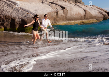 Couple en marche main dans la main à travers le surf sur une plage Banque D'Images