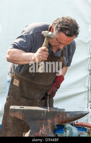 Un forgeron martelant le métal chaud rouge sur une enclume durant une compétition au Royal Cornwall Show 2013 Banque D'Images