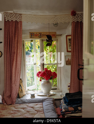 Rideaux rose avec dentelle cantonnières sur fenêtre ouverte avec vase de roses rouges sur le rebord de la fenêtre dans une chambre chalet Banque D'Images