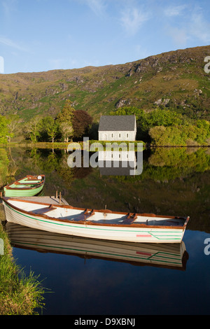 Un bâtiment de l'église blanche sur le bord de l'eau et les canots amarrés dans l'eau ; Gougane Barra, comté de Cork, Irlande Banque D'Images