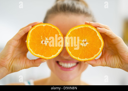 Happy young woman holding deux tranches d'orange en face des yeux Banque D'Images
