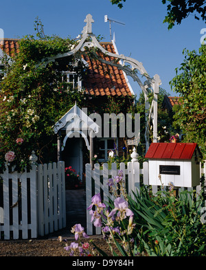 Arche en bois au-dessus du portail blanc en clôture avec postbox blanc en face de chalet avec porche blanc et toit en tuiles rouges Banque D'Images