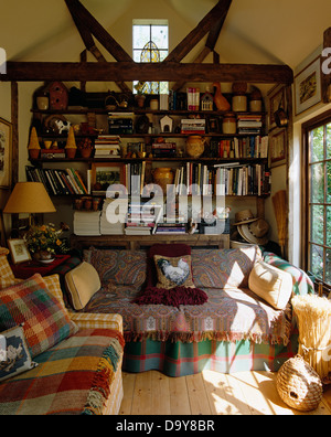 Vérifier et colorés Paisley se jette sur coussins et canapés confortables dans un salon avec bibliothèque et des poutres au plafond de l'apex Banque D'Images